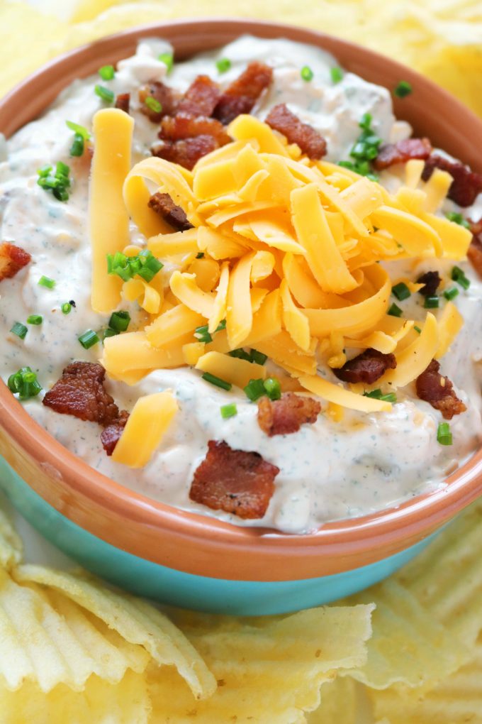 Bacon Cheddar Ranch Dip in an orange and turquoise bowl surrounded by potato chips. 
