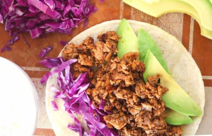 A flat corn tortilla topped and layered with purple cabbage, Chipotle Pork and avocado slices. 
