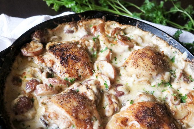 Half of the skillet is showing of the one pot chicken dinner with parsley lying across the top part of the image. 