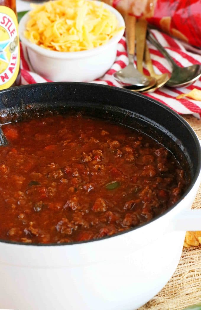 Texas Chili Recipe in a white dutch oven with a small bowl of cheese behind the chili. 