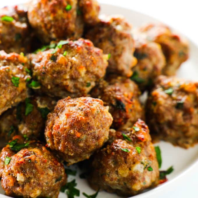 A close up of a plate of Baked Meatballs stacked in a pile.