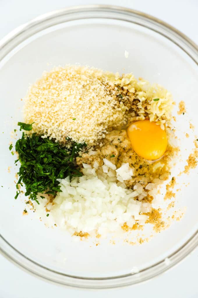 A bowl of breadcrumbs, egg, parsley, onion, and parmesan, not yet mixed together.