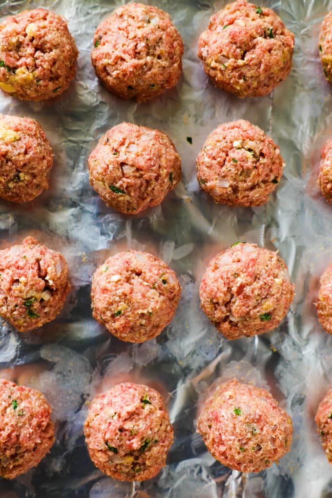 All of the uncooked meatballs lined up on the foil-lined baking sheet.