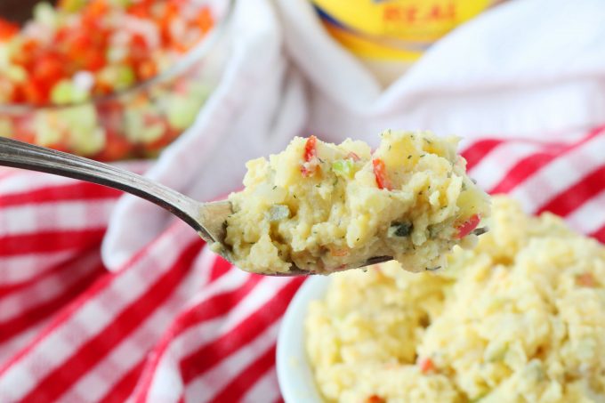 A spoonful of Potato Salad with a red and white checkered tablecloth in the background. 