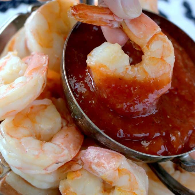 Peeled shrimp surrounding a bowl of cocktail sauce. A shrimp is being dipped into the sauce. 