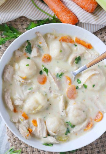 a bowl of chicken and dumplings with carrots and napkins off to the side.