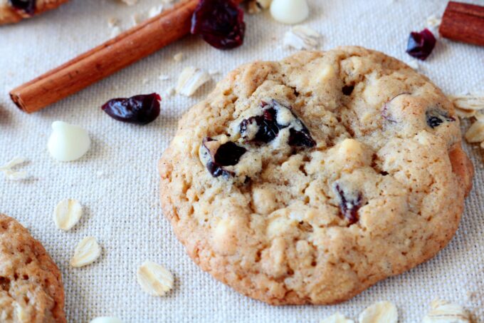 Featuring one oatmeal cookies with cranberries. Surrounding the cookie are a cinnamon stick, cranberries, and oats. 