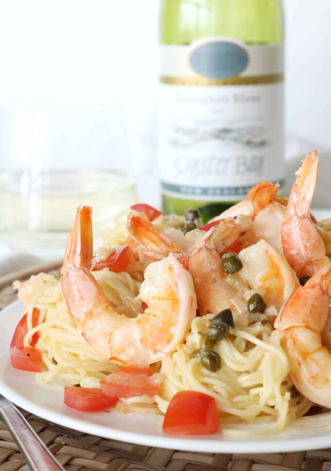 Shrimp pasta on a white plate with a stemless glass of white wine in the background along with the bottle of wine. 