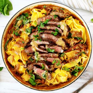 And overhead shot of steak pasta in a braiser dish with strips of steak lining the center.