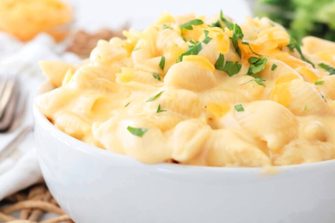 A close up shot of a bowl of Shells and Cheese with parsley garnished on top. 