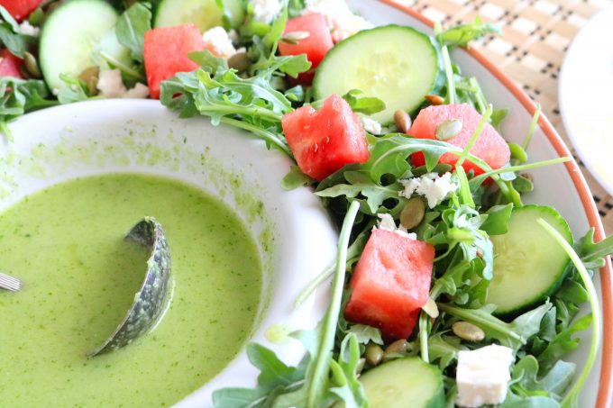 A close up shot of a bowl of Serrano Lime Dressing surrounded by watermelon arugula salad. 