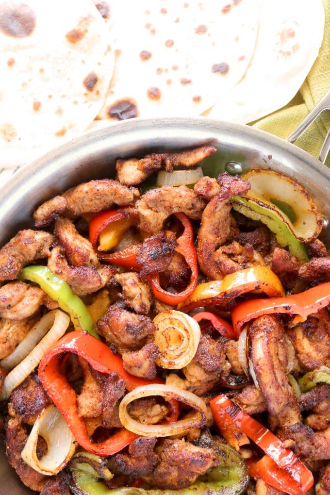 Skillet Chicken Fajitas in a skillet surrounded by flour tortillas sitting off to the side. 