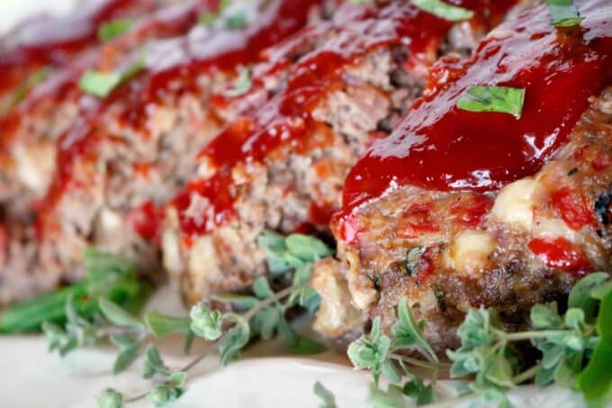 A close up shot of Italian Meatloaf on a white serving dish. Fresh thyme sprigs are placed around the meatloaf. 
