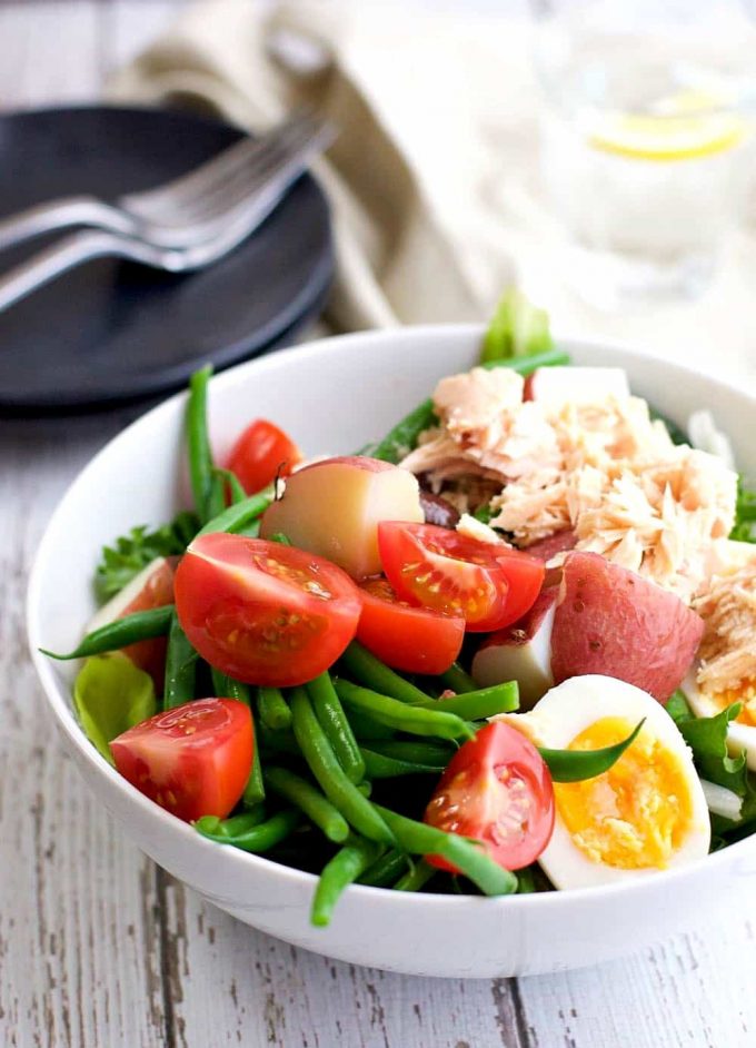 A green bean salad with canned tuna, tomatoes, hard boiled egg all served in a white bowl. 