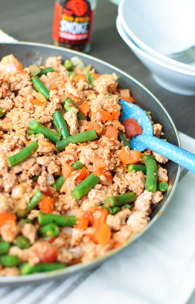 A skillet of ground turkey and green beans with a blue spoon resting in the dish. 
