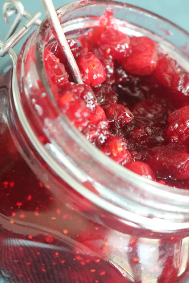 A close up shot of cranberry relish in a clear glass jar. 