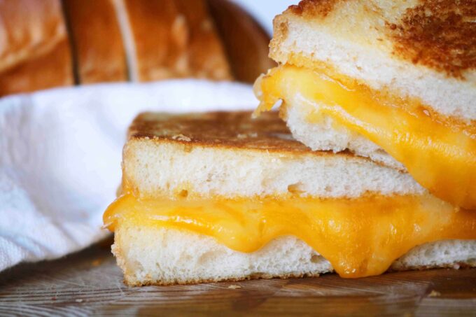 Two pieces of grilled cheese stacked on top of each other. The cheese in the center is melting between the two slices of toasted white bread. 