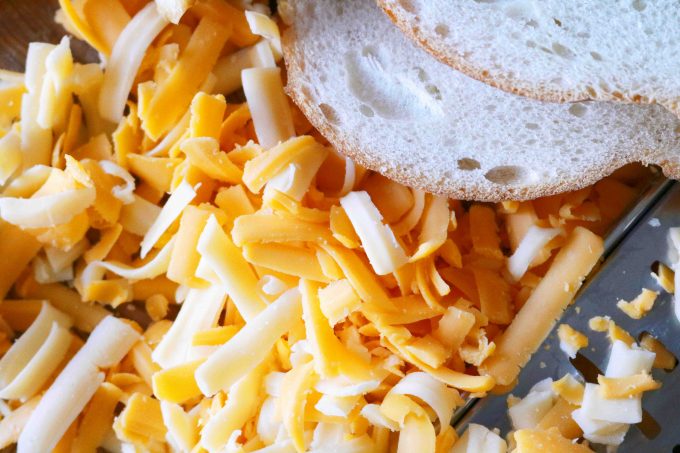 An overhead shot of shredded havarti and cheddar Cheese lying next two slices of white bread. 