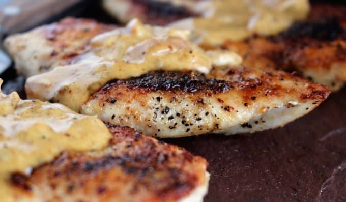 Seared chicken breast topped with the mustard cream curry sauce sitting on top of a dark plate. 