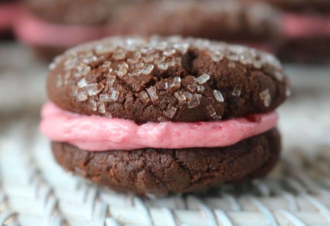 A close up shot of two chocolate wafers sandwiched between a raspberry filling. The cookie is sitting on top of a white placemat. 