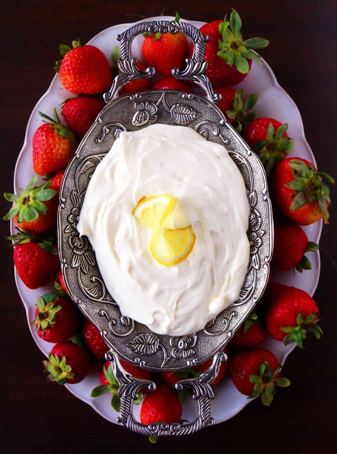 An overhead shot of of a serving platter of yogurt fruit dip that is placed in the center of a larger white serving dish. The fruit dip bowl is surrounded by whole fresh strawberries. 