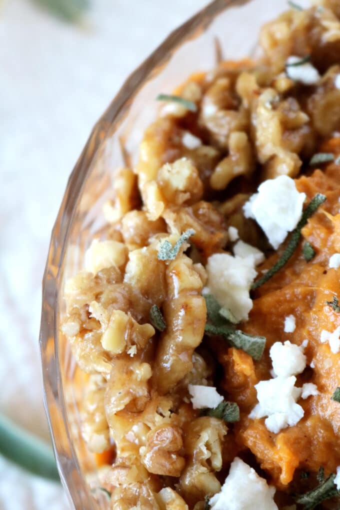 A close up shot of sprinkled goat cheese, fresh herbs and walnuts sitting on top of the mashed sweet potatoes. 