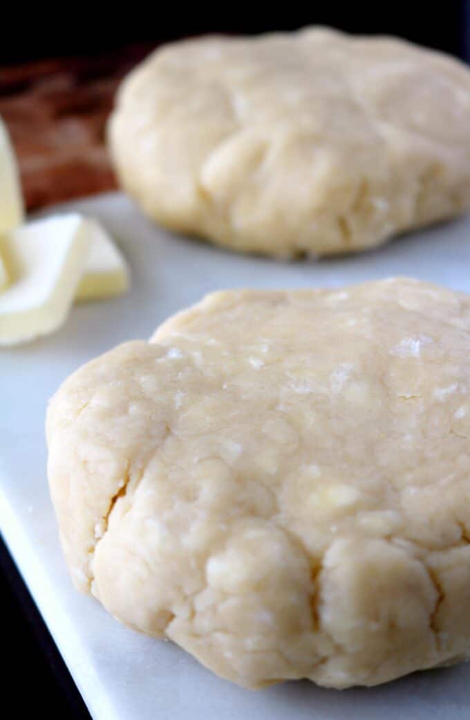 Two dough rounds sitting on a white cutting board with slices of butter in the top left corner. 