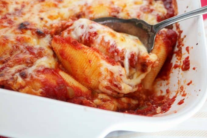 A white baking dish that is full of easy stuffed shells with ricotta cheese, Fontina and Parmesan. A serving spoon is being scooped underneath one of the shells. 