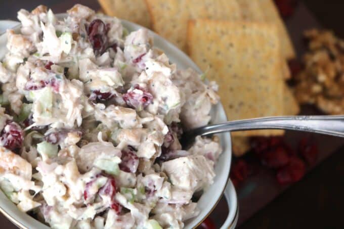 A white bowl of turkey salad with a silver spoon resting in the salad. Off to the side are a couple of crackers. 
