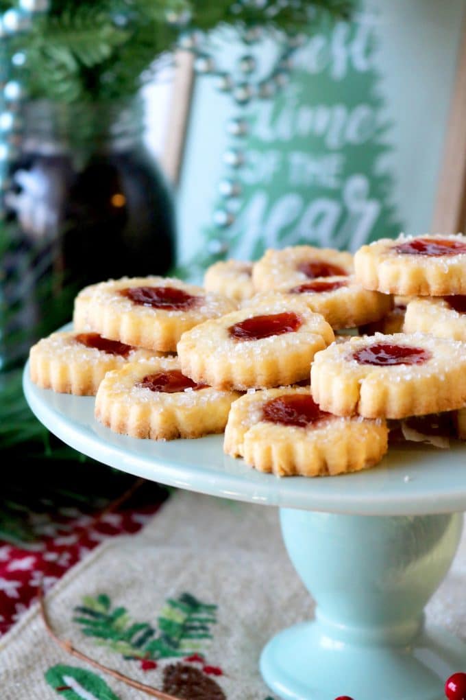 Strawberry Butter Jam Thumbprint Cookies on a light blue cake stand. Behind the plate of cookies are Christmas decorations and greenery. 