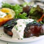 Grilled steak topped with creamy horseradish sauce served with a baked potato and green salad