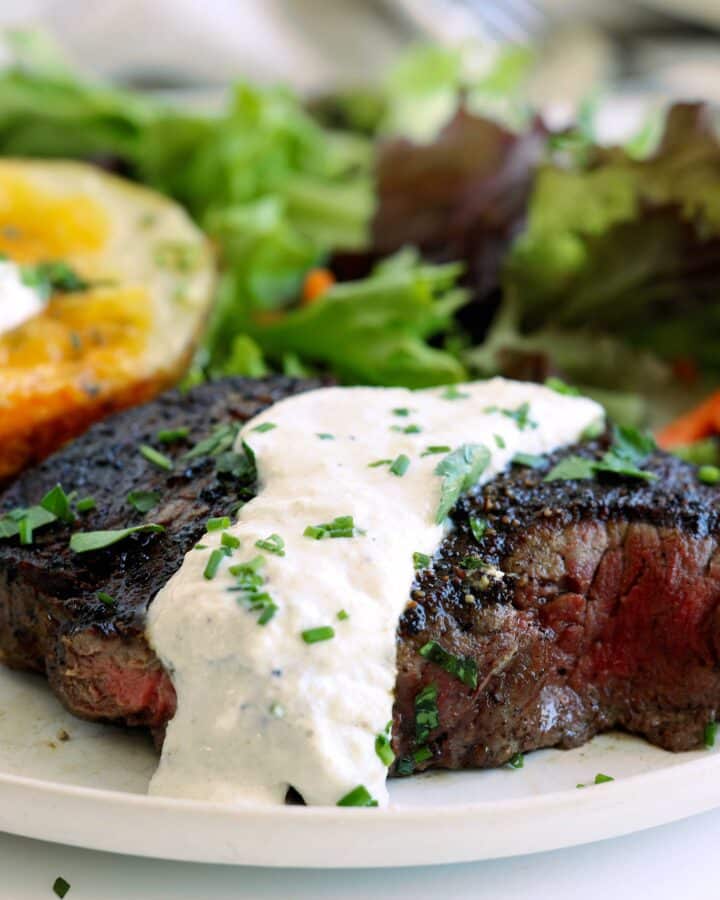 Grilled steak topped with creamy horseradish sauce served with a baked potato and green salad