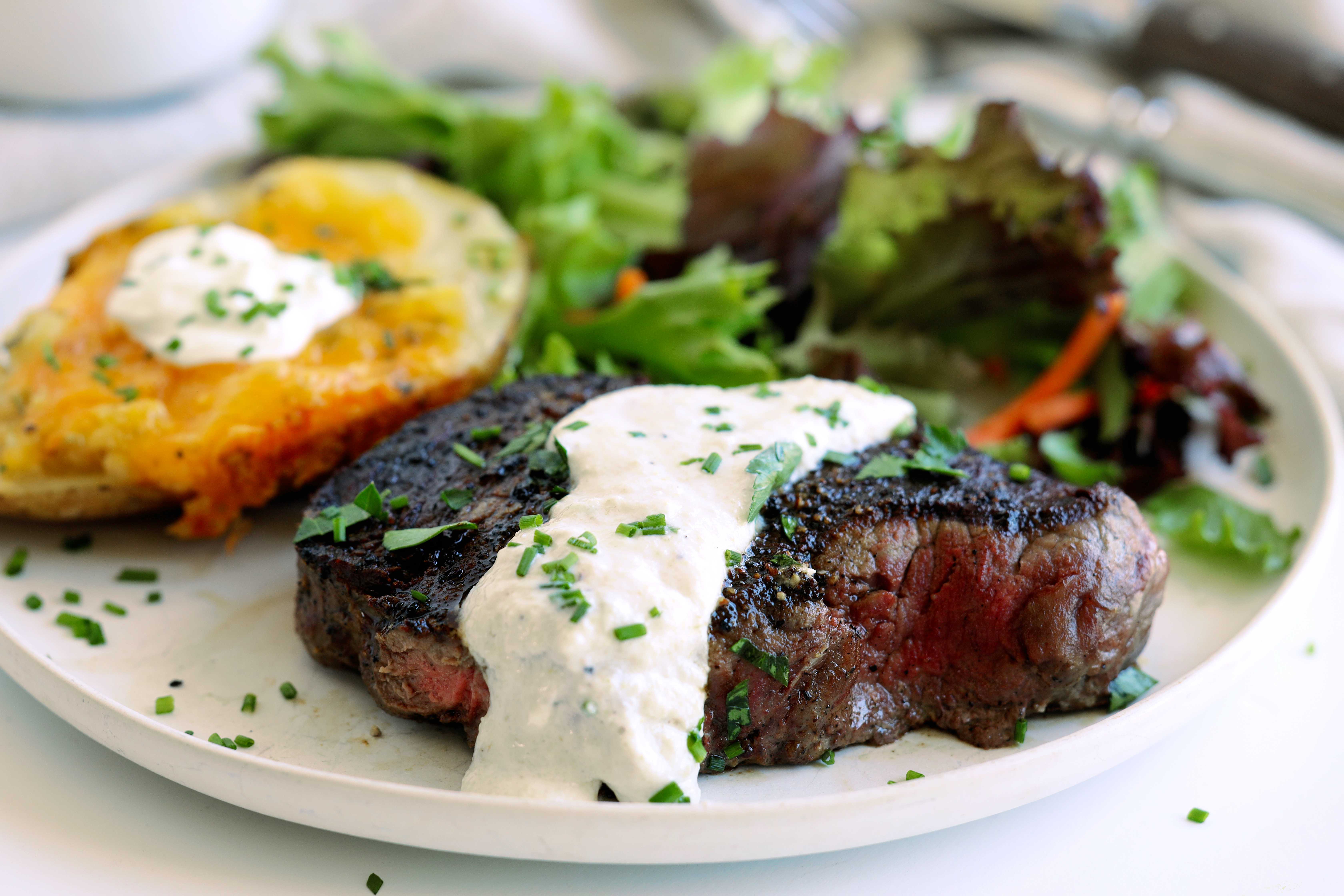 Grilled steak topped with creamy horseradish sauce served with a baked potato and green salad