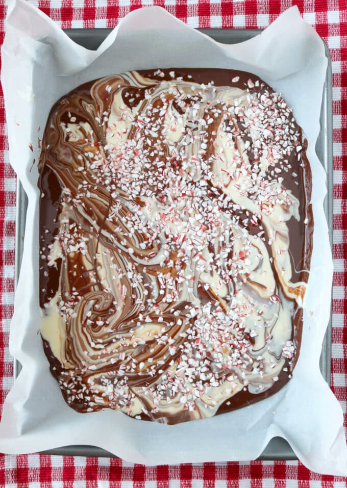 Chocolate Peppermint Bark in a rectangular baking dish that is lined with parchment paper. The dish is sitting on top of a red and white checkered tablecloth. 
