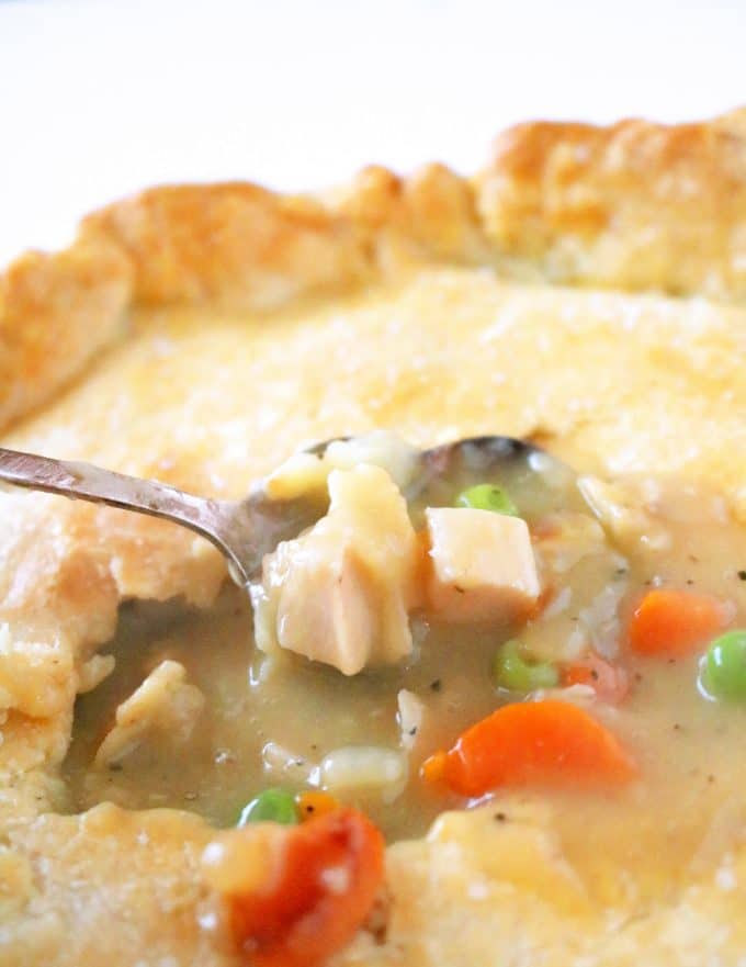 A close up shot of a spoon being dipped in the center of chicken pot pie. 