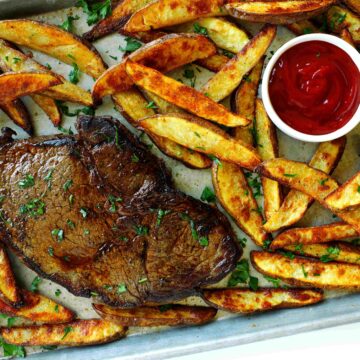 Ribeye steak served with crispy homemade steak fries and ketchup on a sheet pan, garnished with parsley.