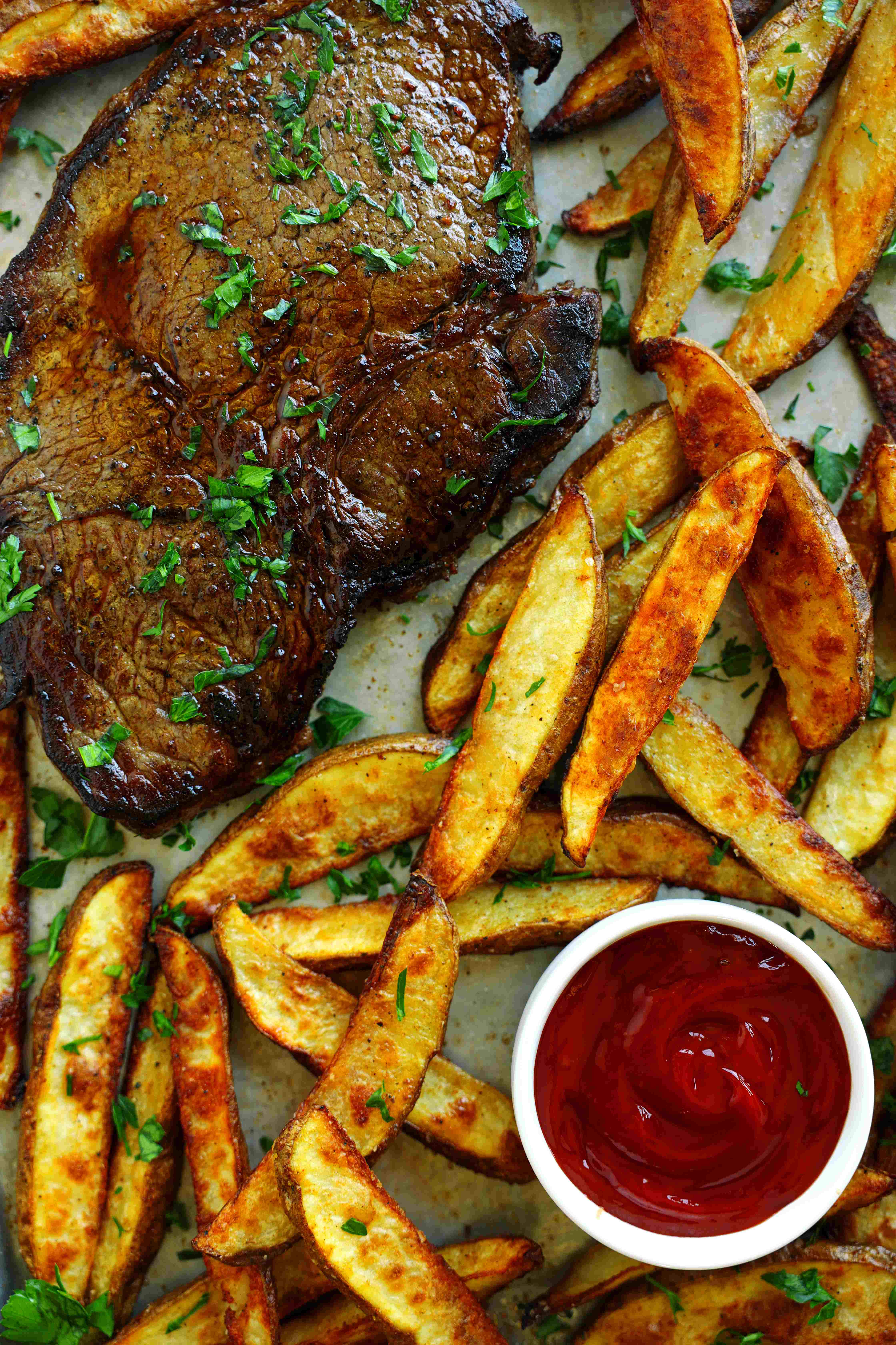 Juicy steak served with crispy oven-baked steak fries and ketchup, garnished with fresh parsley.