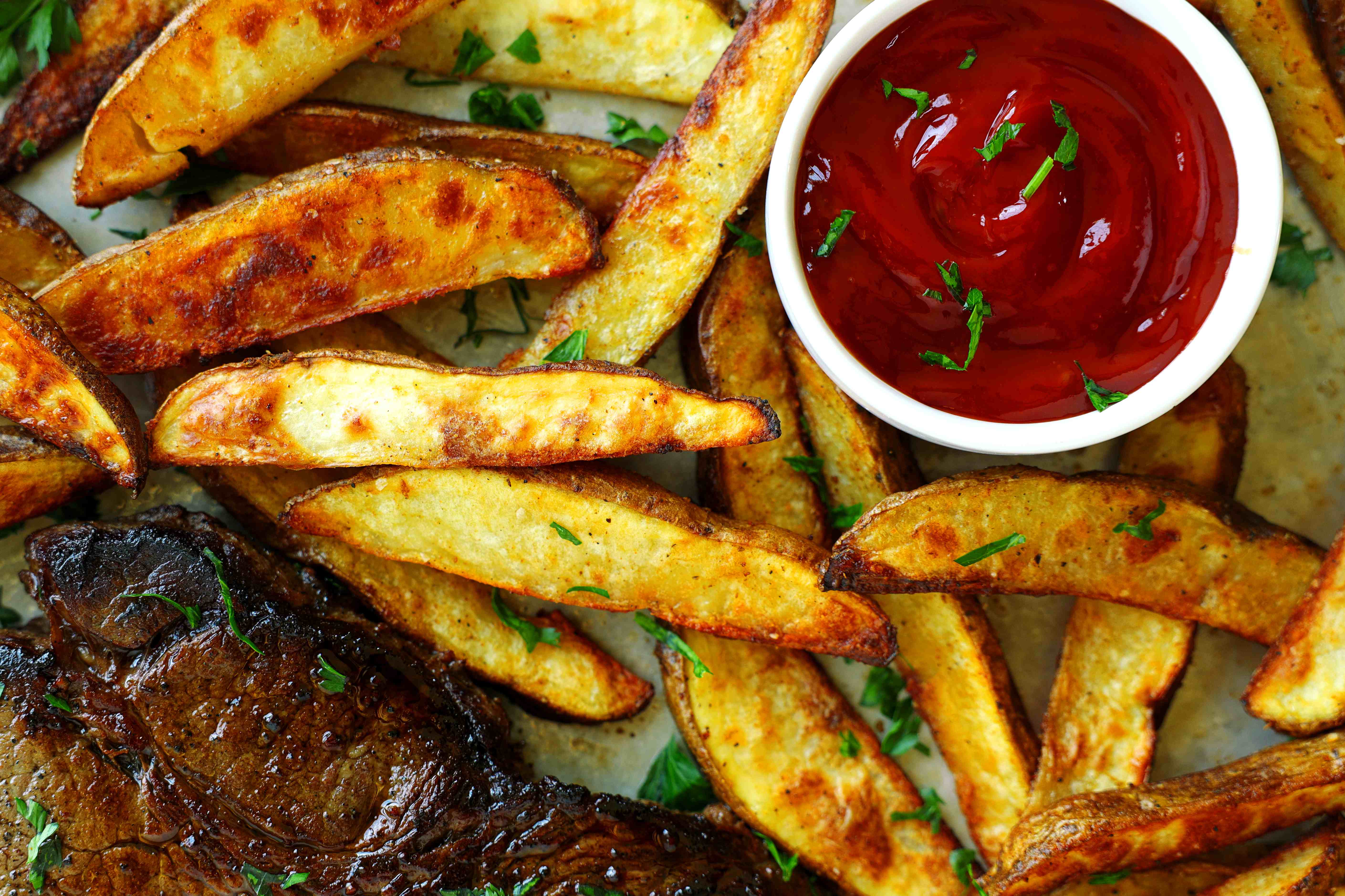 Crispy oven-baked steak fries served with ketchup and steak, garnished with fresh parsley.