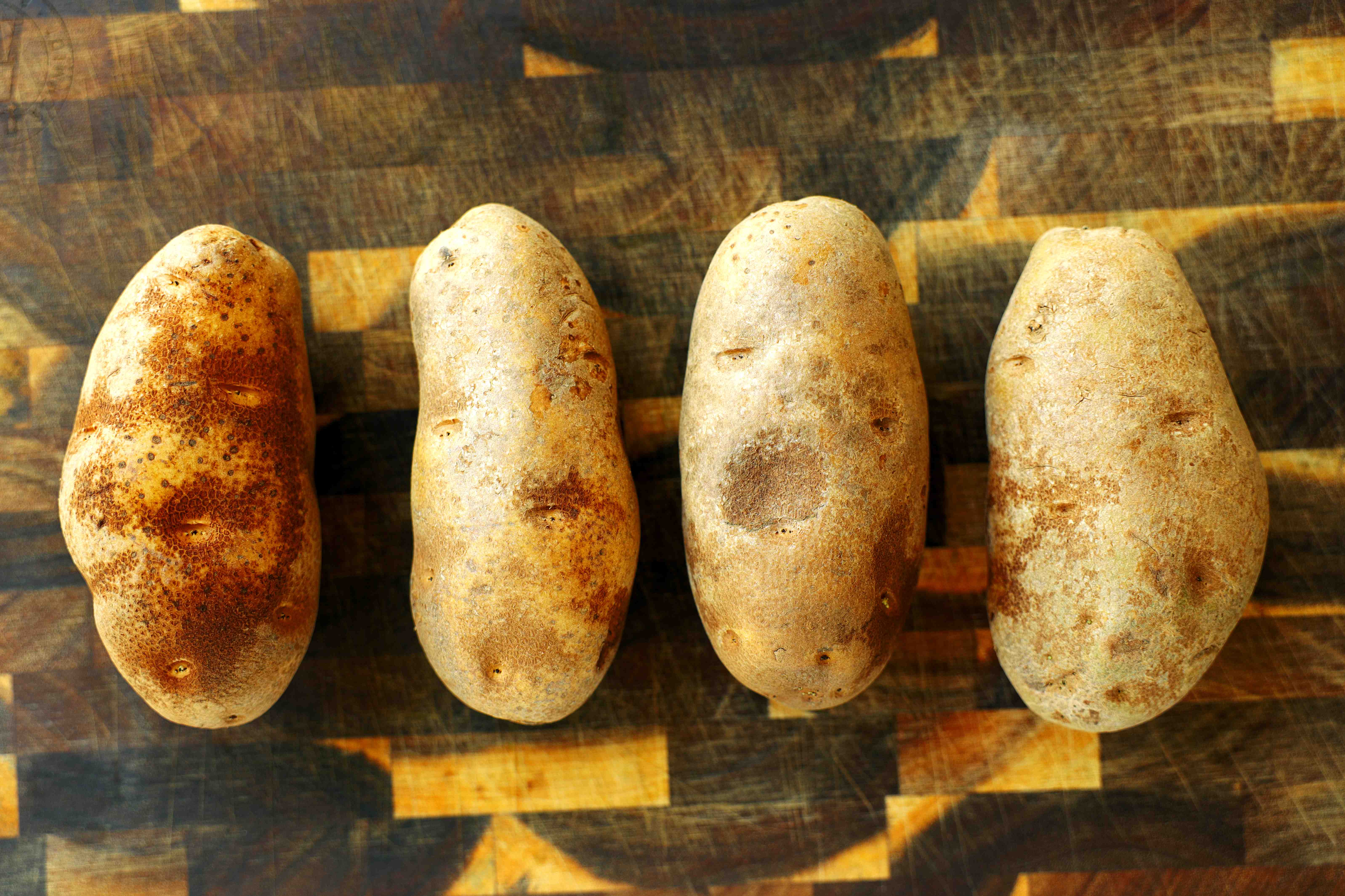 Russet potatoes cut into thick wedges on a wooden cutting board for homemade steak fries.