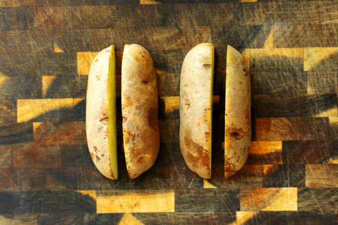 Russet potatoes sliced in half on a wooden cutting board before cutting into steak fries.