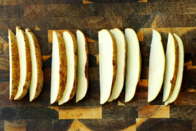 Whole russet potatoes on a wooden cutting board for making crispy oven-baked steak fries.