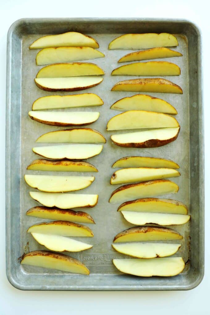 Raw russet potato wedges arranged in a single layer on a sheet pan for homemade steak fries.