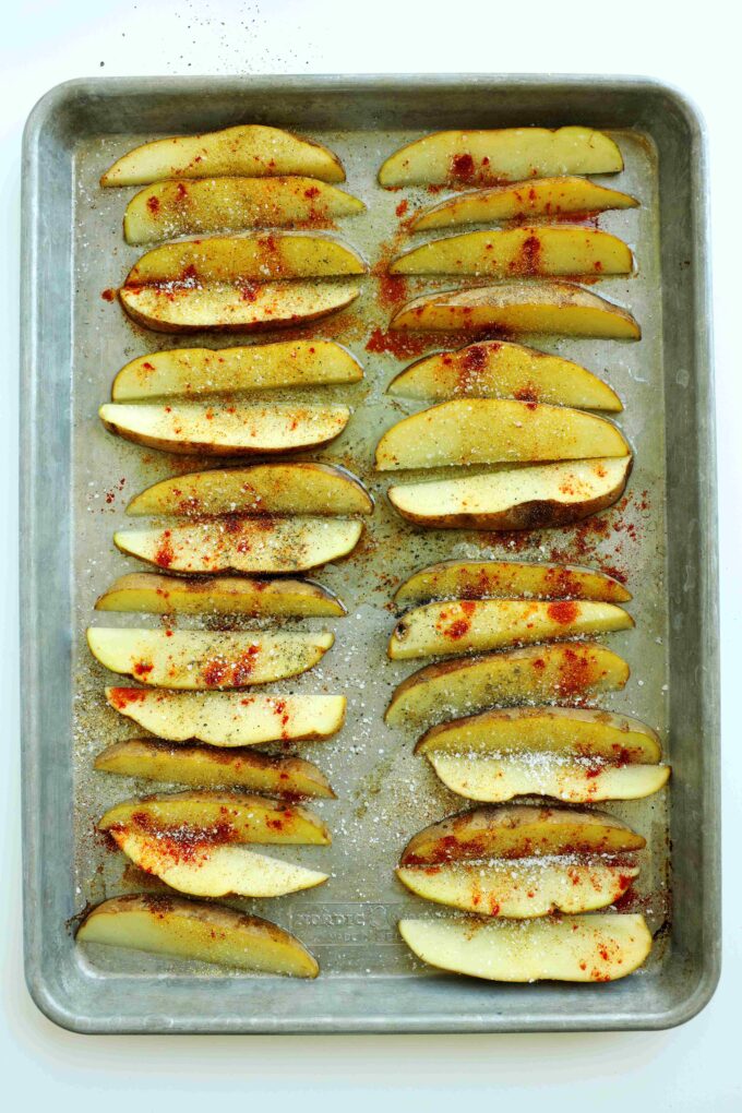 Steak fries seasoned with salt, pepper, and paprika on a baking sheet before roasting.