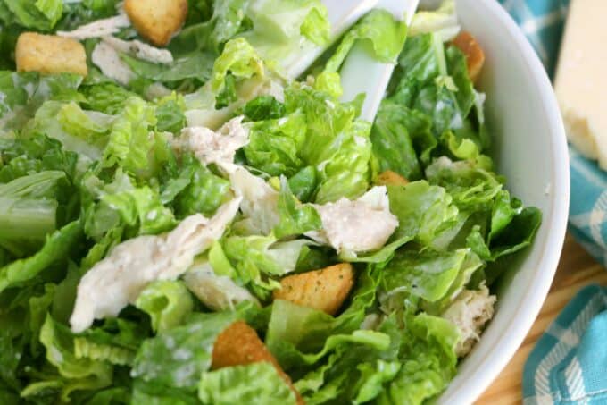 Shredded Chicken sitting on a bed of romaine lettuce with a couple of crouton sprinkled in. The salad is in a white serving bowl. 
