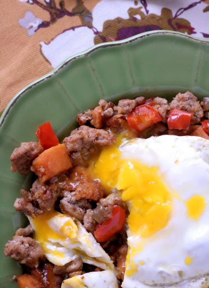 Sweet potato turkey hash with fried egg on top being served on a green scalloped plate. 