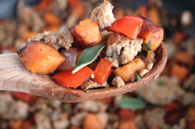 A wooden spoon of sweet potato turkey hash being held over a dish full of hash. 