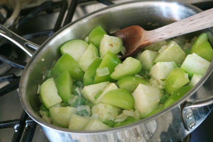 Quartered tomatillos and diced onions cooking in a saucepan. 