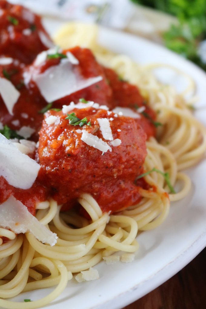 A close up shot of spaghetti and meatballs served in a white shallow bowl. The dish is sprinkled with freshly shaved parmesan. 
