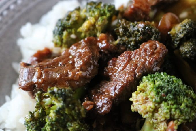 A close up shot of beef and broccoli stir fry served on top of white rice. 