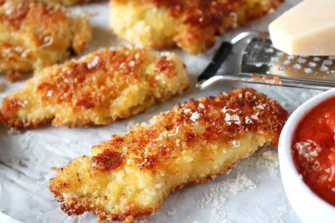 These photo features parmesan crusted chicken tenders with a cheese grater and a block of parmesan cheese. 